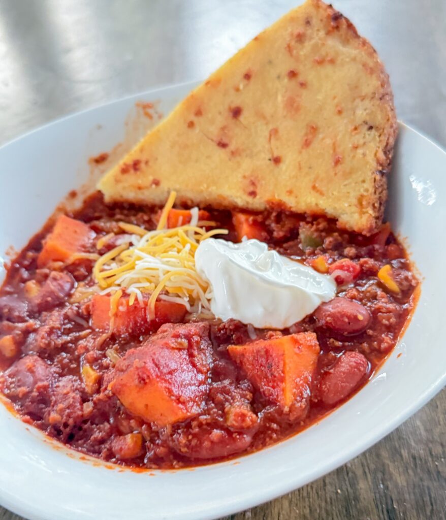 Sweet potato turkey chili topped with shredded cheese and sour cream, served with a slice of cornbread.